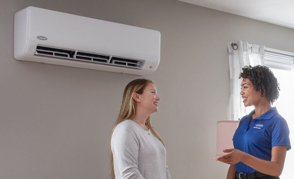 Female Dealer Talking To Female Customer In Room Ductless HVAC On Wall